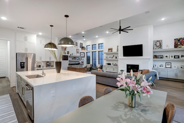 kitchen featuring sink, decorative light fixtures, a center island with sink, stainless steel appliances, and white cabinets