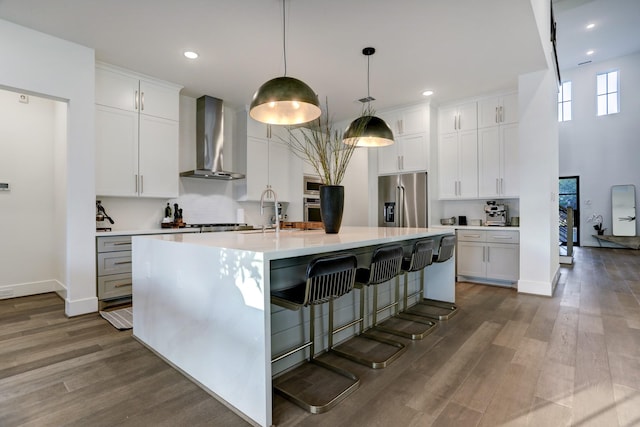 kitchen with white cabinets, an island with sink, wall chimney exhaust hood, and appliances with stainless steel finishes