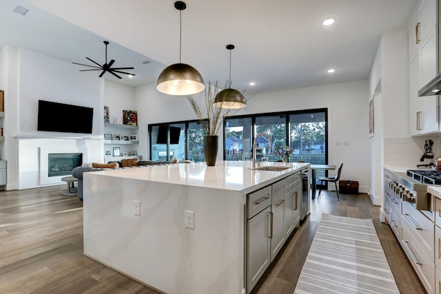 kitchen with sink, hanging light fixtures, a center island with sink, dark hardwood / wood-style flooring, and decorative backsplash