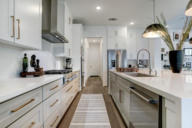 kitchen with sink, decorative light fixtures, wall chimney range hood, stainless steel appliances, and white cabinets