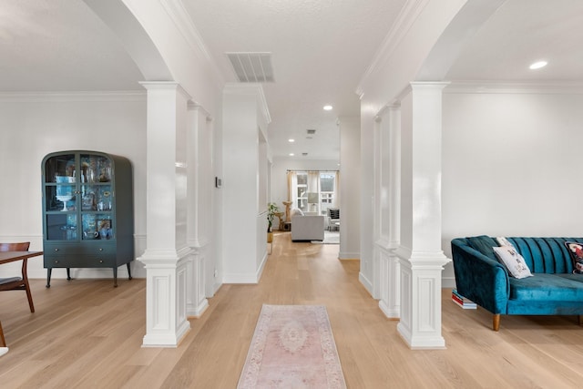 hall with ornate columns, ornamental molding, and light hardwood / wood-style flooring