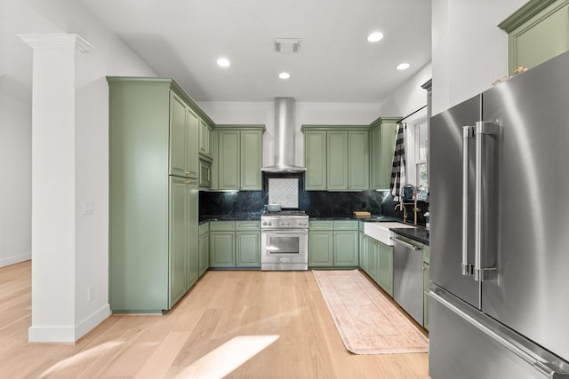 kitchen featuring high end appliances, wall chimney range hood, sink, and green cabinets