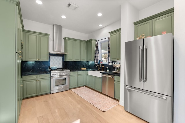 kitchen featuring high quality appliances, sink, light wood-type flooring, and wall chimney exhaust hood