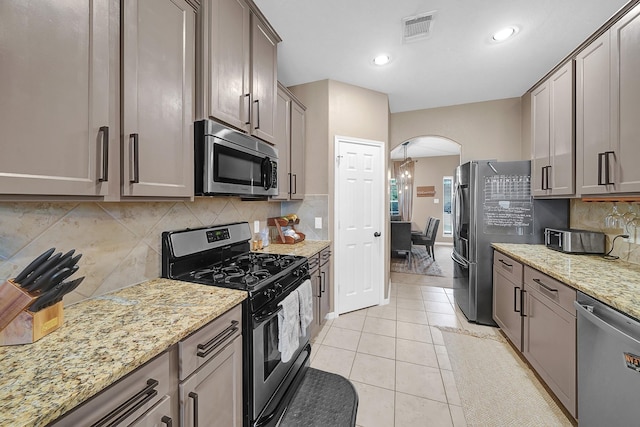 kitchen featuring light stone counters, stainless steel appliances, decorative backsplash, and light tile patterned floors