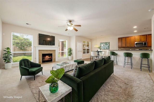 living room featuring ceiling fan, a tiled fireplace, and light carpet