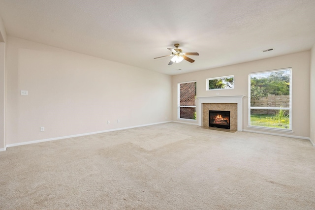 unfurnished living room featuring ceiling fan, light colored carpet, a tile fireplace, and a textured ceiling