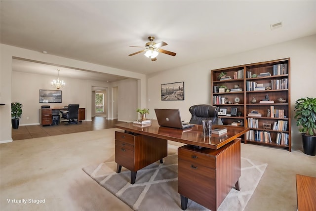 carpeted office space featuring ceiling fan with notable chandelier