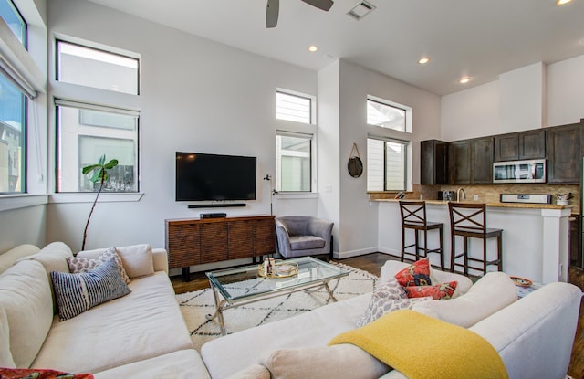 living room featuring a high ceiling, ceiling fan, and light hardwood / wood-style flooring