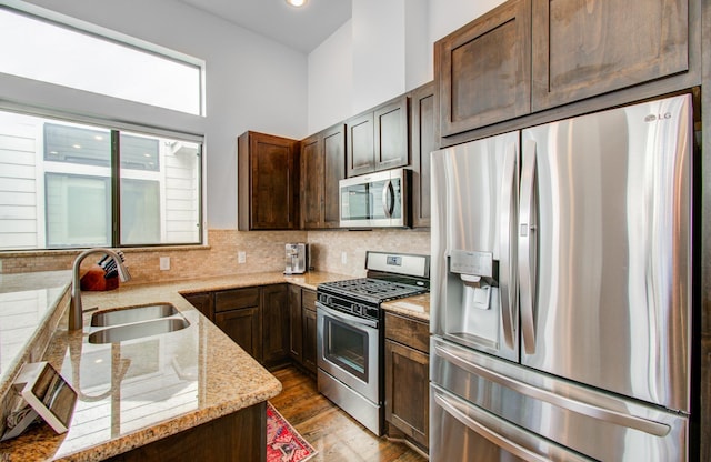 kitchen with appliances with stainless steel finishes, sink, decorative backsplash, light hardwood / wood-style floors, and light stone countertops