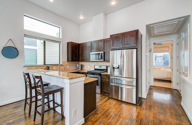 kitchen with a breakfast bar, stainless steel appliances, tasteful backsplash, light stone countertops, and kitchen peninsula