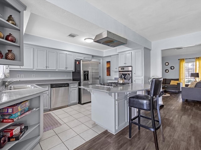 kitchen featuring open shelves, stainless steel appliances, visible vents, a sink, and a kitchen breakfast bar