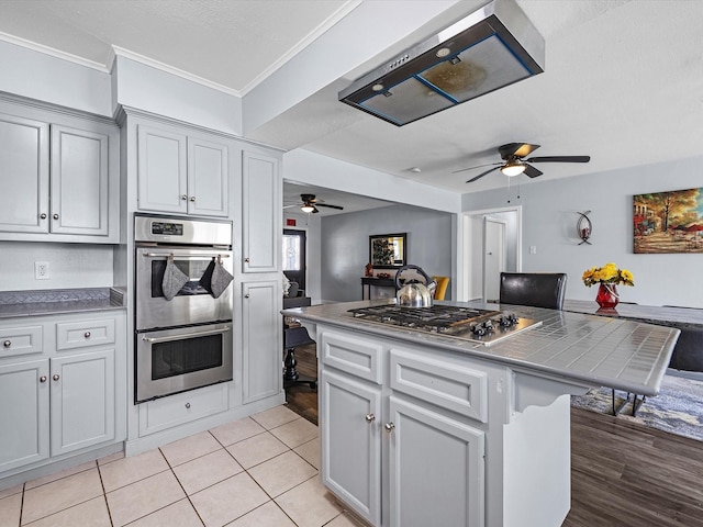 kitchen featuring light tile patterned floors, a ceiling fan, open floor plan, stainless steel appliances, and crown molding