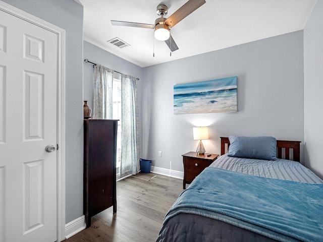 bedroom featuring a ceiling fan, visible vents, baseboards, and wood finished floors