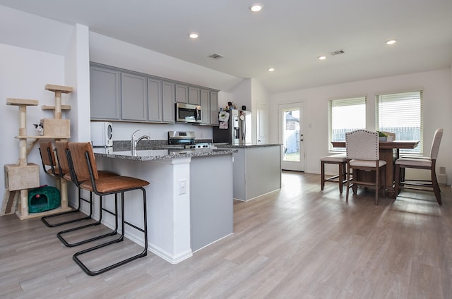 kitchen featuring a center island with sink, light wood-type flooring, dark stone counters, gray cabinets, and stainless steel appliances