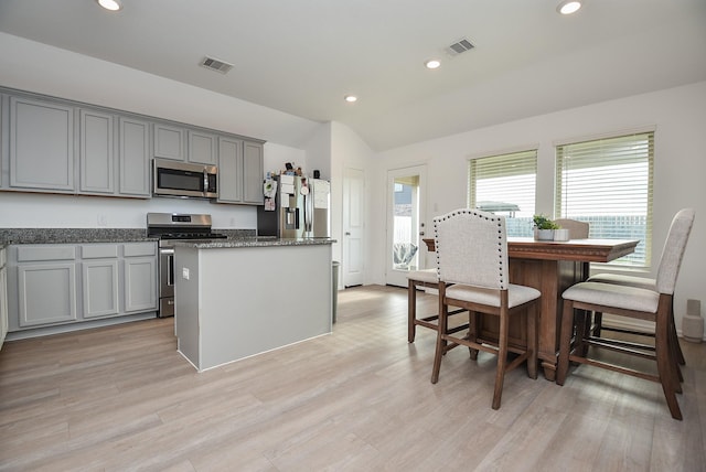 kitchen with dark stone countertops, appliances with stainless steel finishes, gray cabinets, a kitchen island, and light hardwood / wood-style floors