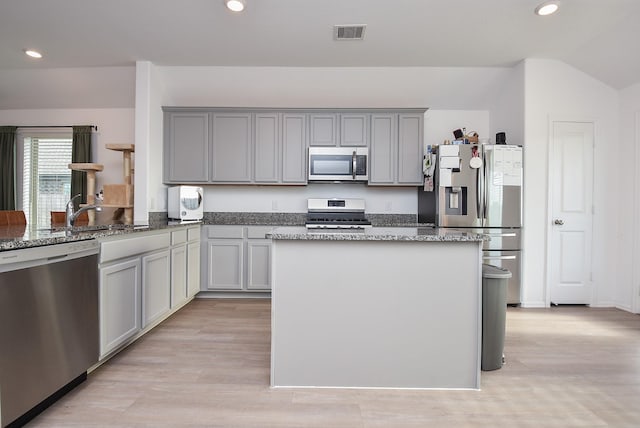 kitchen with dark stone countertops, light wood-type flooring, gray cabinets, and appliances with stainless steel finishes