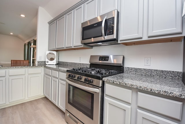 kitchen with light hardwood / wood-style flooring, light stone countertops, vaulted ceiling, and appliances with stainless steel finishes