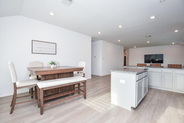 kitchen with light stone counters, vaulted ceiling, light hardwood / wood-style floors, and a kitchen island