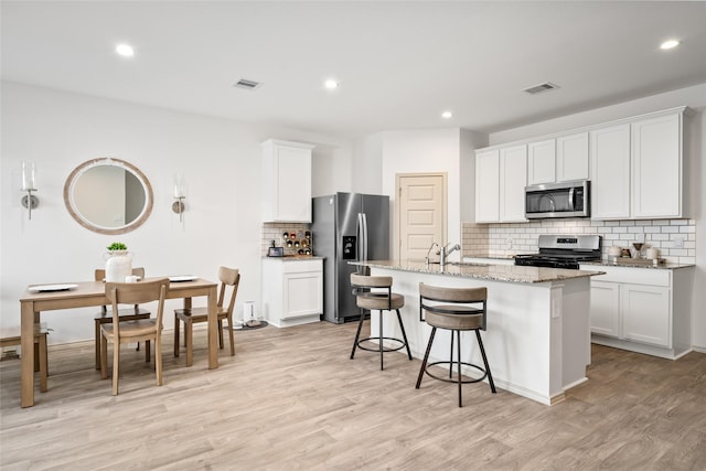 kitchen with stainless steel appliances, a center island with sink, and white cabinets