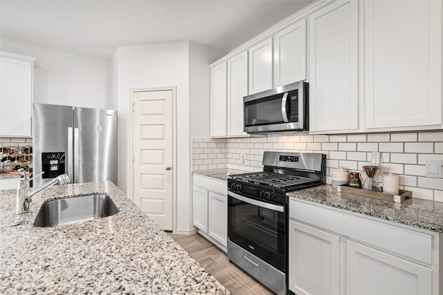 kitchen with backsplash, white cabinetry, stainless steel appliances, and a sink