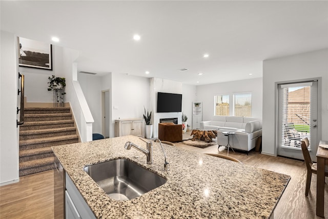 kitchen featuring recessed lighting, a fireplace, a sink, light wood-style floors, and light stone countertops