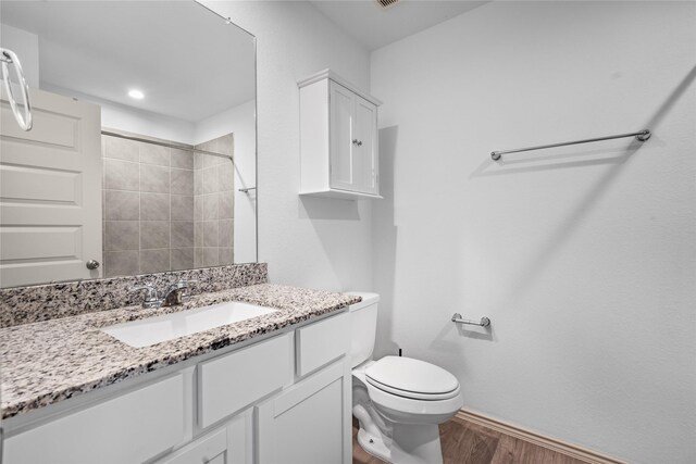 bathroom featuring a tile shower, vanity, wood-type flooring, and toilet