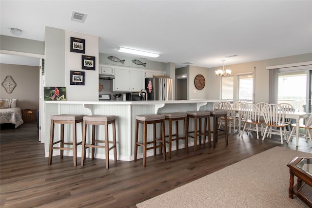 kitchen with stainless steel fridge, white cabinetry, hanging light fixtures, dark hardwood / wood-style floors, and kitchen peninsula