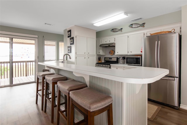 kitchen with appliances with stainless steel finishes, a breakfast bar, white cabinetry, dark hardwood / wood-style flooring, and a center island