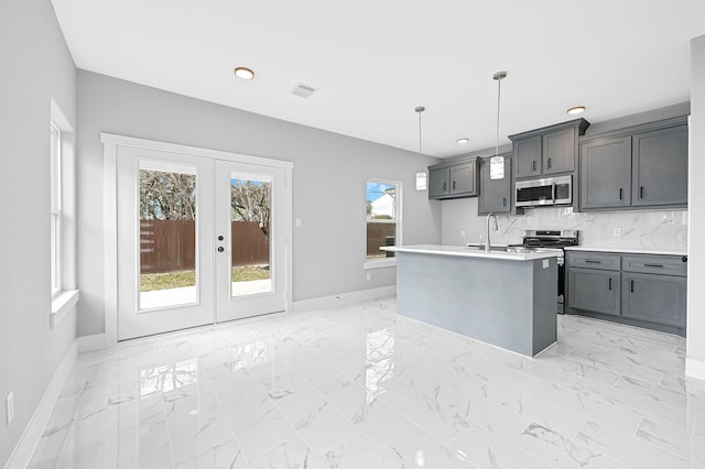 kitchen featuring appliances with stainless steel finishes, hanging light fixtures, tasteful backsplash, a center island with sink, and french doors