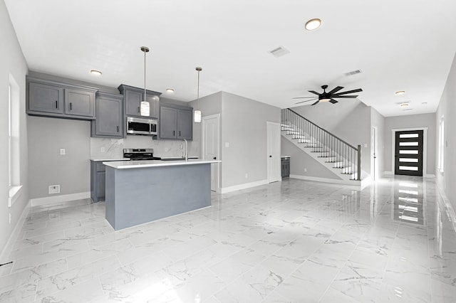 kitchen with pendant lighting, ceiling fan, appliances with stainless steel finishes, gray cabinetry, and an island with sink