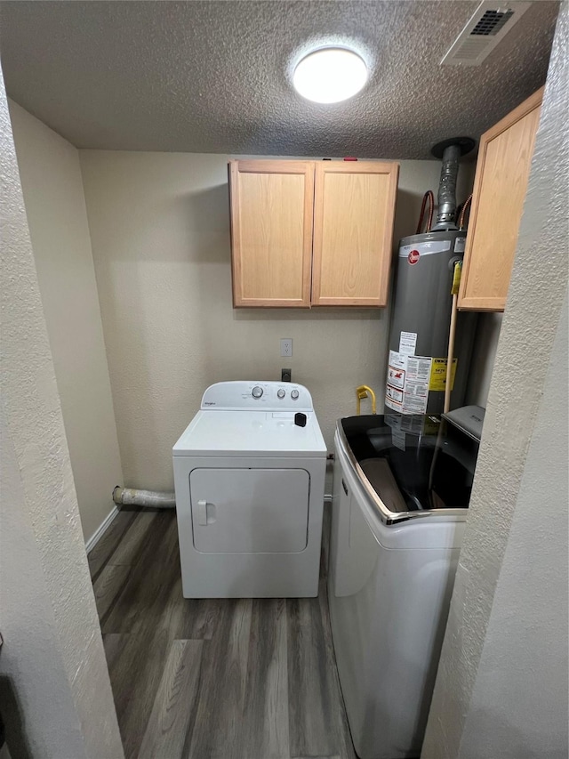 clothes washing area featuring water heater, washing machine and dryer, cabinets, dark hardwood / wood-style floors, and a textured ceiling