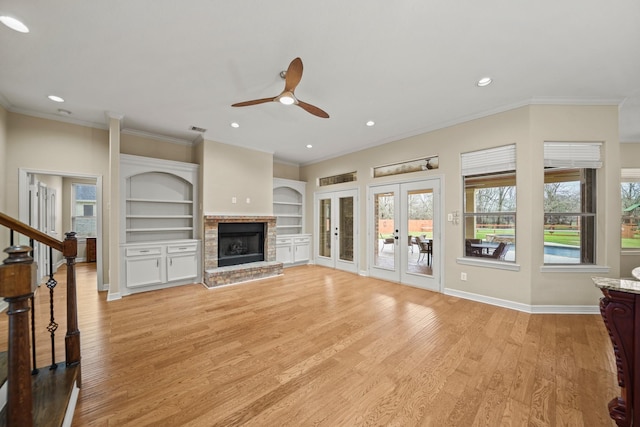 unfurnished living room with ceiling fan, light wood-style flooring, ornamental molding, a brick fireplace, and french doors