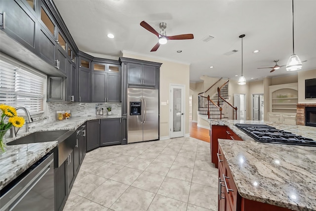 kitchen with appliances with stainless steel finishes, hanging light fixtures, dark brown cabinets, light stone counters, and a kitchen island