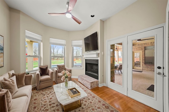 living area with ceiling fan, a fireplace, light wood-style flooring, and baseboards
