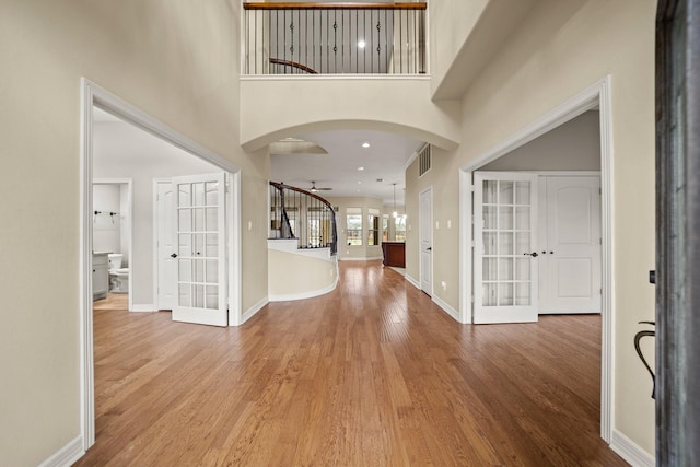 foyer entrance with french doors, arched walkways, wood finished floors, baseboards, and a towering ceiling