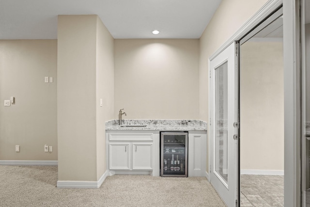 bar featuring wine cooler, sink, light stone counters, light carpet, and white cabinets