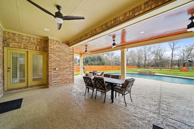 view of patio / terrace with a ceiling fan, outdoor dining area, fence, a playground, and a pool with connected hot tub