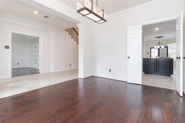 unfurnished dining area featuring ornate columns, wood-type flooring, ornamental molding, and an inviting chandelier