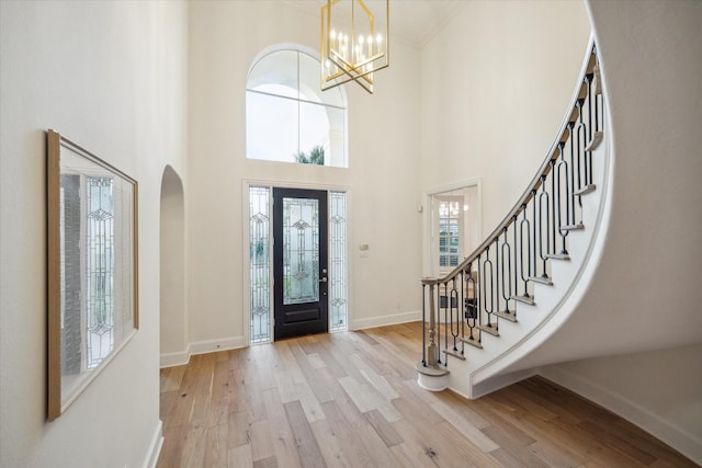 entrance foyer featuring a high ceiling, crown molding, a notable chandelier, and light hardwood / wood-style flooring