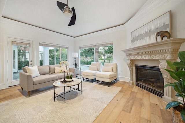 living room featuring crown molding, a fireplace, ceiling fan, and light wood-type flooring