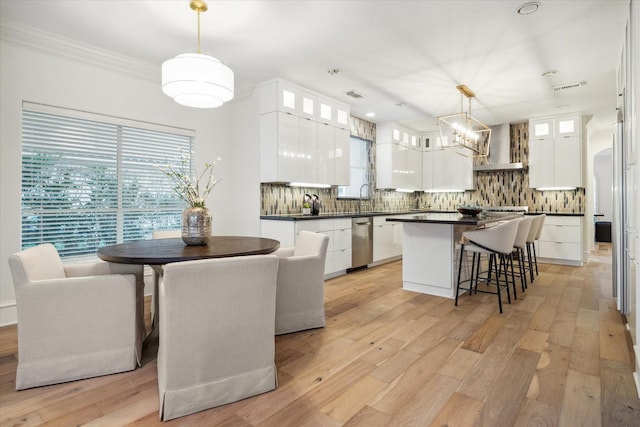 kitchen with white cabinetry, decorative backsplash, hanging light fixtures, a center island, and wall chimney range hood