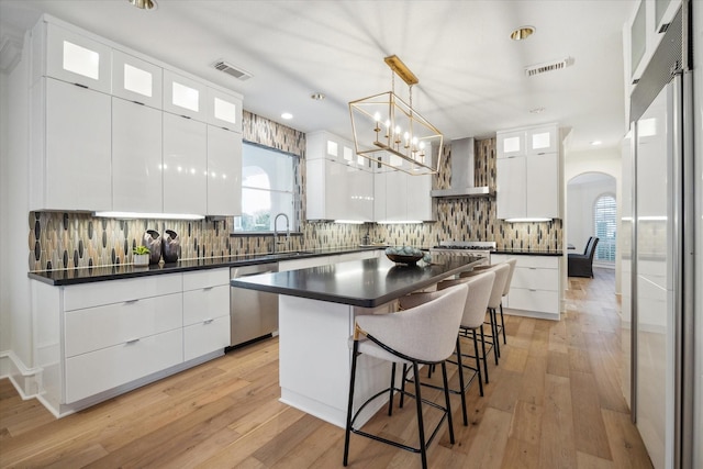 kitchen featuring wall chimney exhaust hood, dishwasher, a kitchen island, and white cabinets