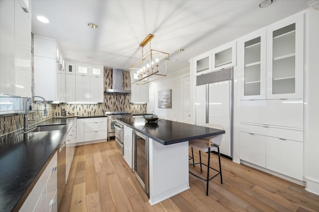 kitchen with sink, white cabinetry, a center island, high quality appliances, and wall chimney range hood