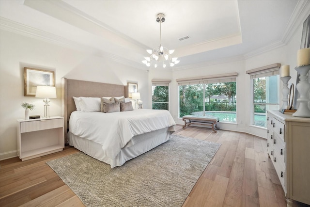 bedroom with ornamental molding, an inviting chandelier, light wood-type flooring, and a tray ceiling