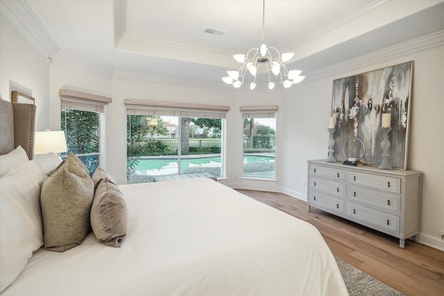 bedroom featuring ornamental molding, light hardwood / wood-style flooring, a notable chandelier, and a tray ceiling