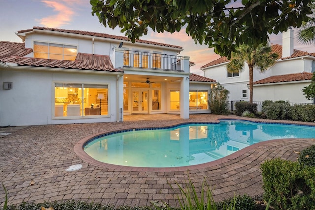 pool at dusk featuring ceiling fan and a patio area