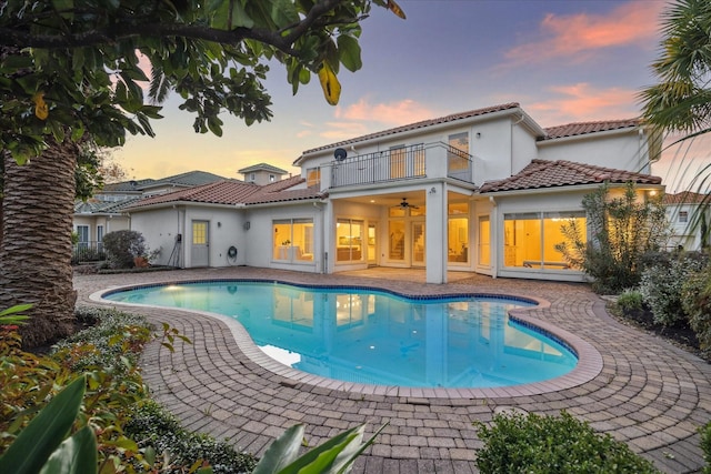 pool at dusk with a patio and ceiling fan