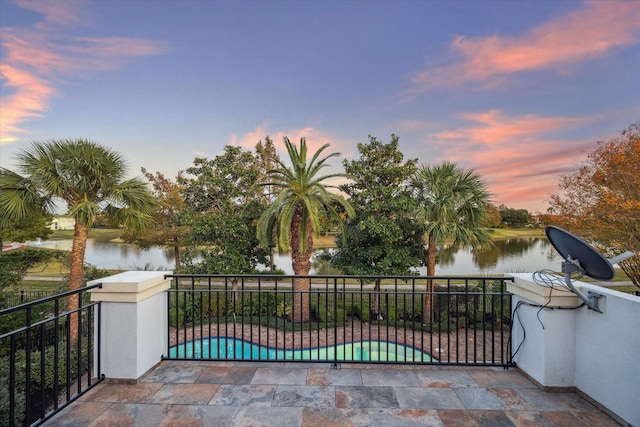 patio terrace at dusk with a fenced in pool, a balcony, and a water view