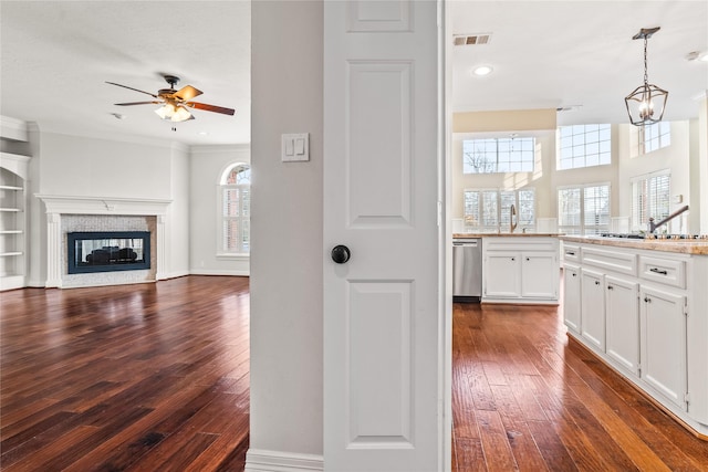 kitchen with a multi sided fireplace, dark hardwood / wood-style floors, pendant lighting, white cabinets, and stainless steel dishwasher