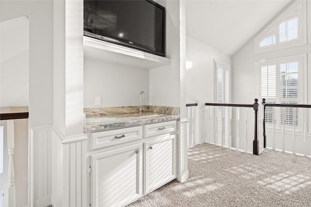 kitchen featuring lofted ceiling, sink, white cabinets, light stone counters, and light carpet